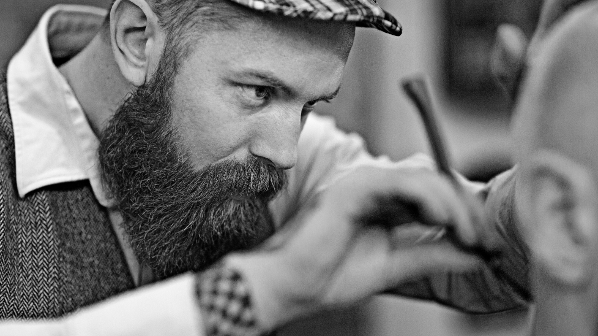 الحلاق يقوم بحلاقة دقيقة باستخدام ماكينة حلاقة مستقيمة بشفرة حلاقة ذات حافة واحدة على العميل.